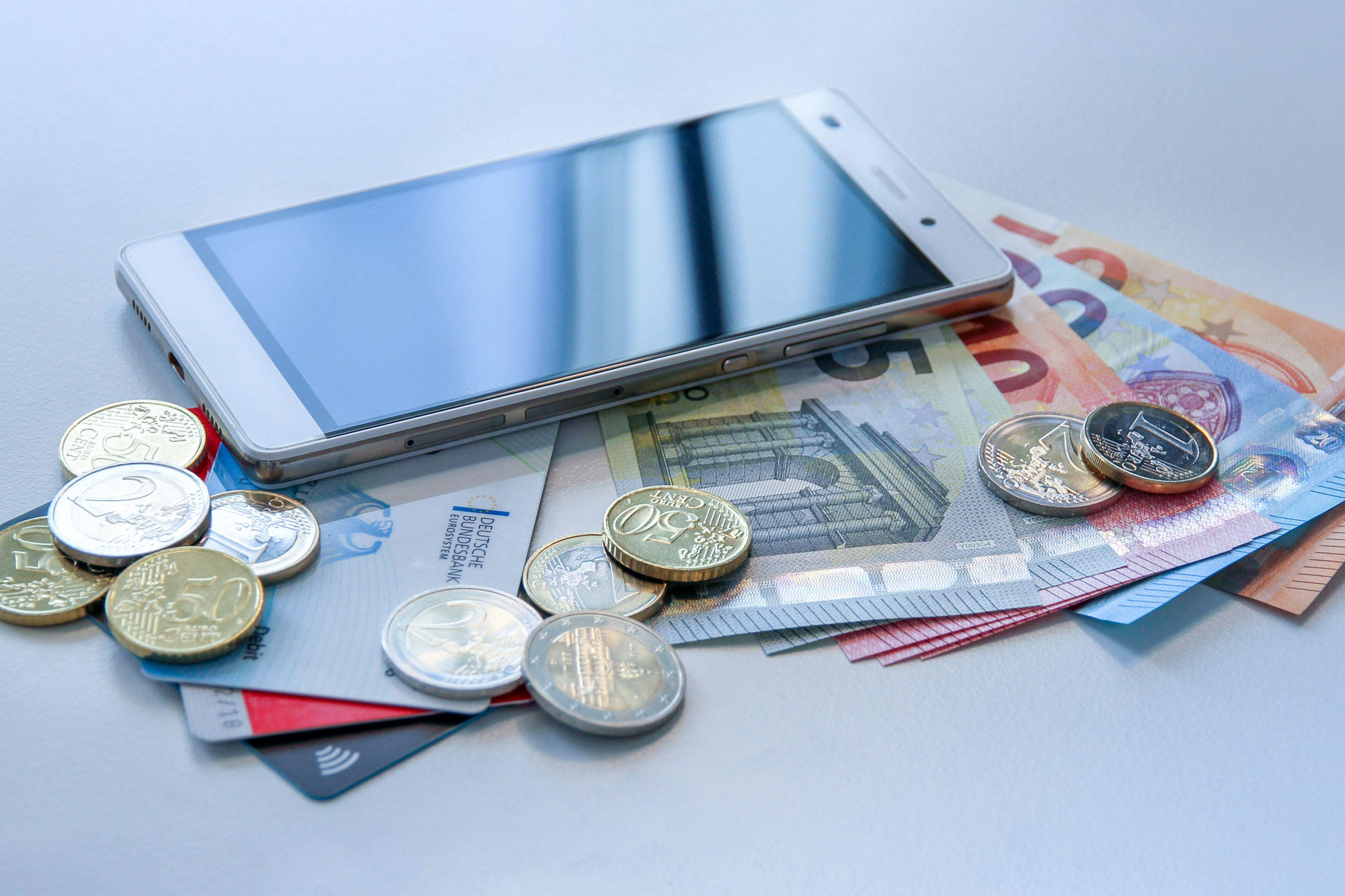 Ein Smartphone, Bargeld und Karten als Zahlungsmittel
